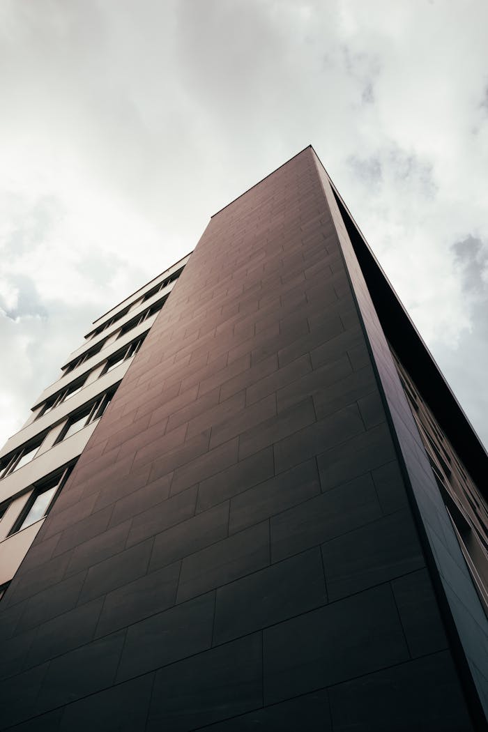 Contact A powerful angle capturing a towering modern building against a cloudy sky, showcasing urban architectural design.