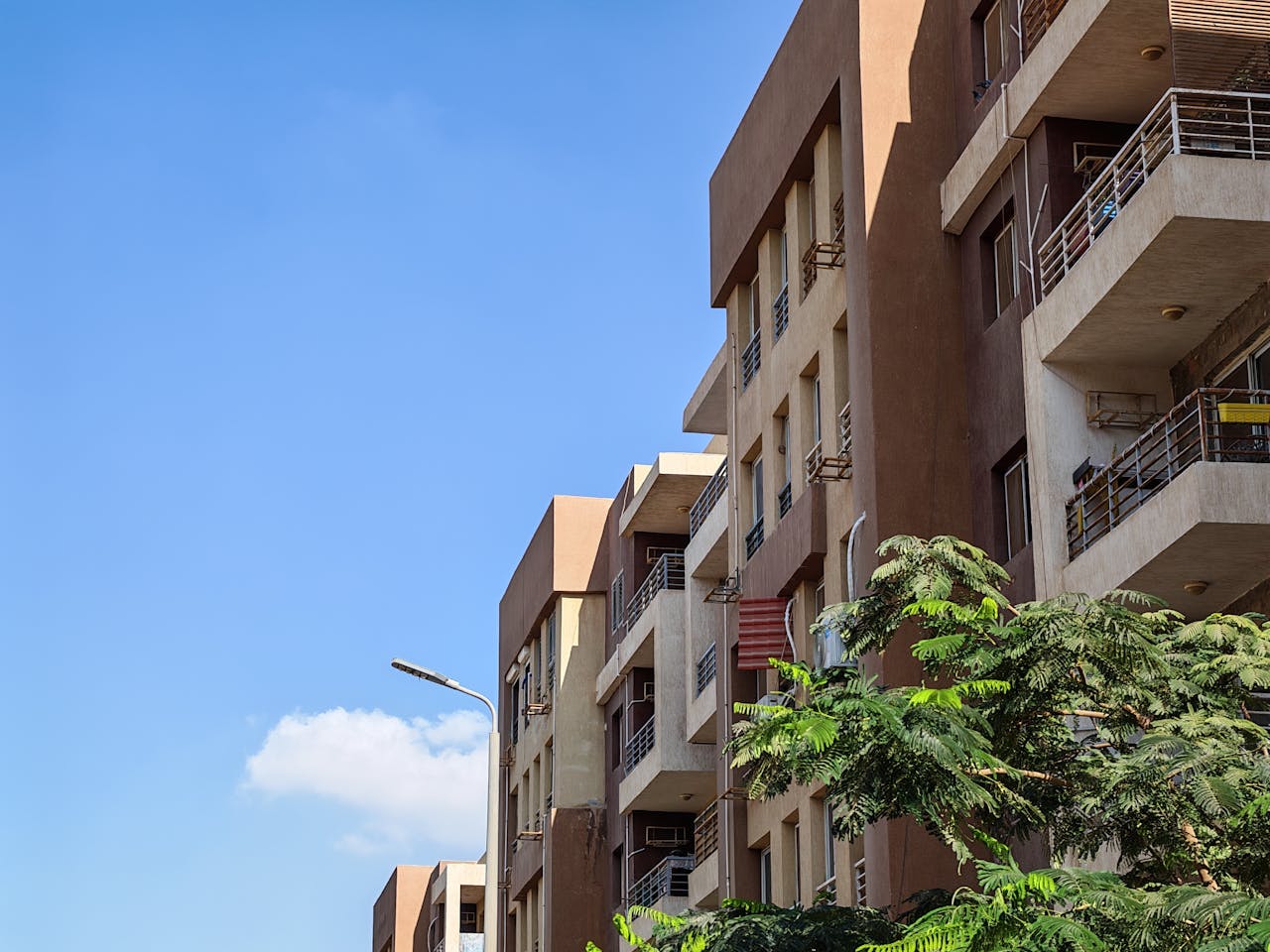 Home Urban apartment building against a bright blue sky with foliage in the foreground.